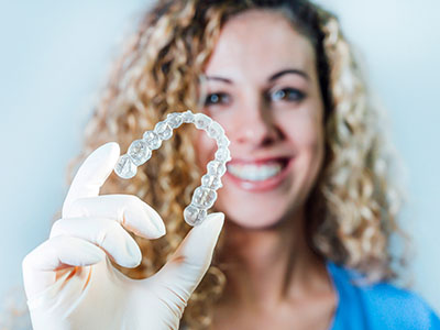 A person wearing a blue surgical mask holds up an intricate, clear dental implant mold with a smile.