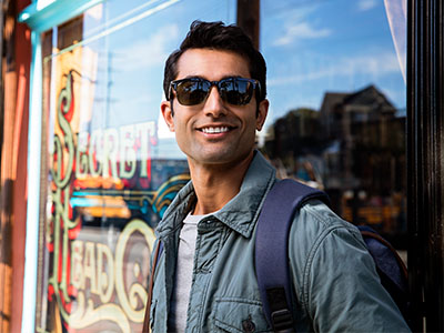 A young man with sunglasses stands in front of a storefront, smiling and posing for the camera.