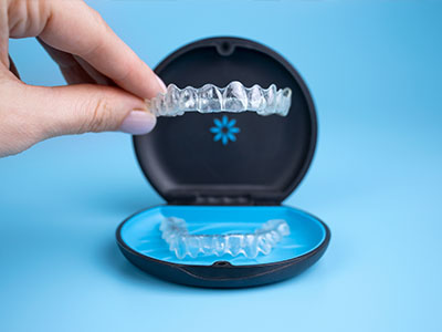 The image shows a hand holding an open clear case containing a set of transparent dental aligners, with the brand name Invisalign visible on the case.
