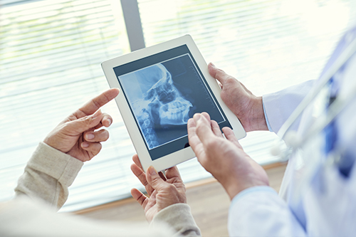A medical professional interacting with a tablet displaying an X-ray, assisted by another individual in a healthcare setting.